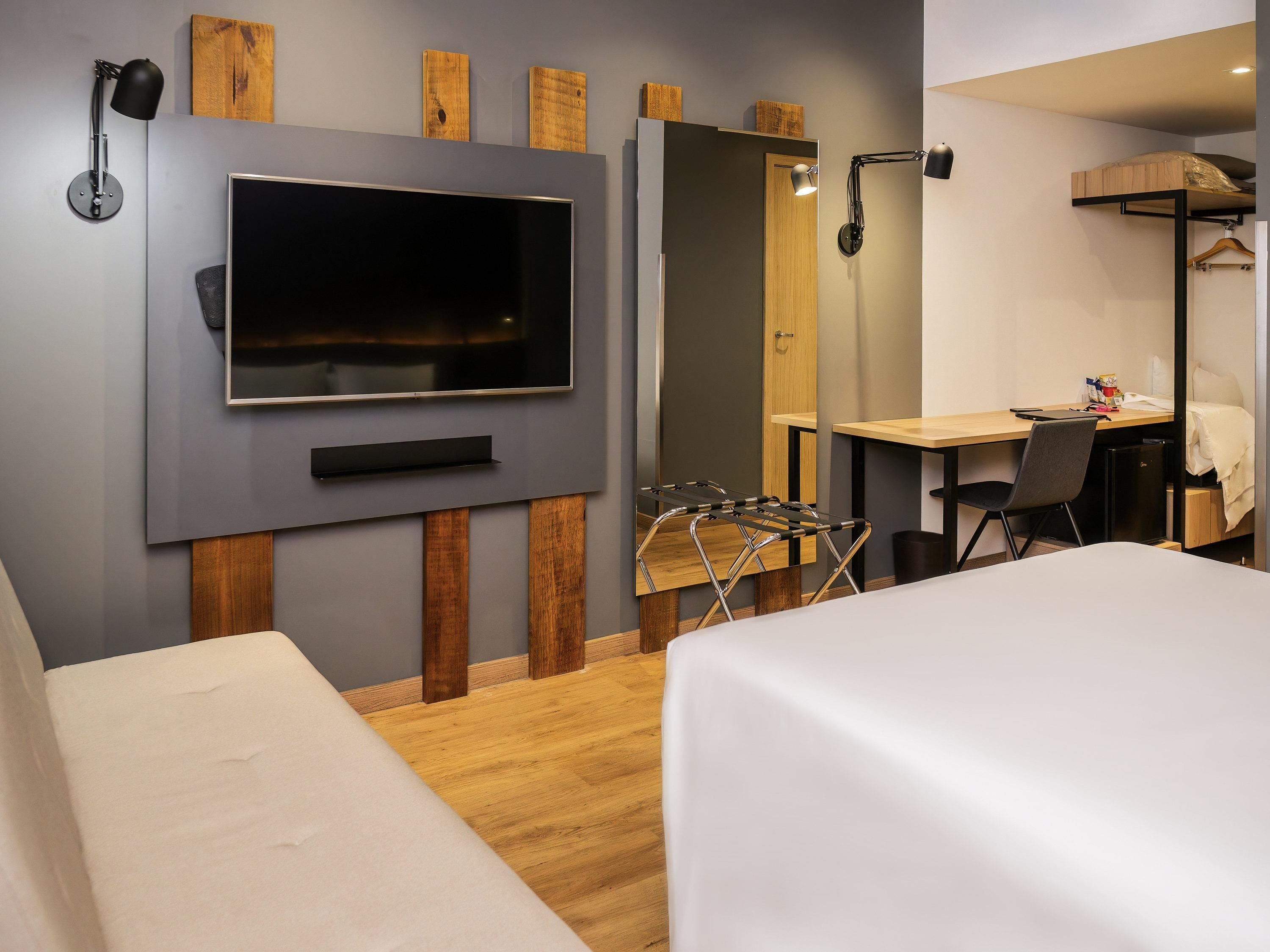 A modern hotel room with a flat-screen TV, a desk with a chair, a bed, and a wardrobe.