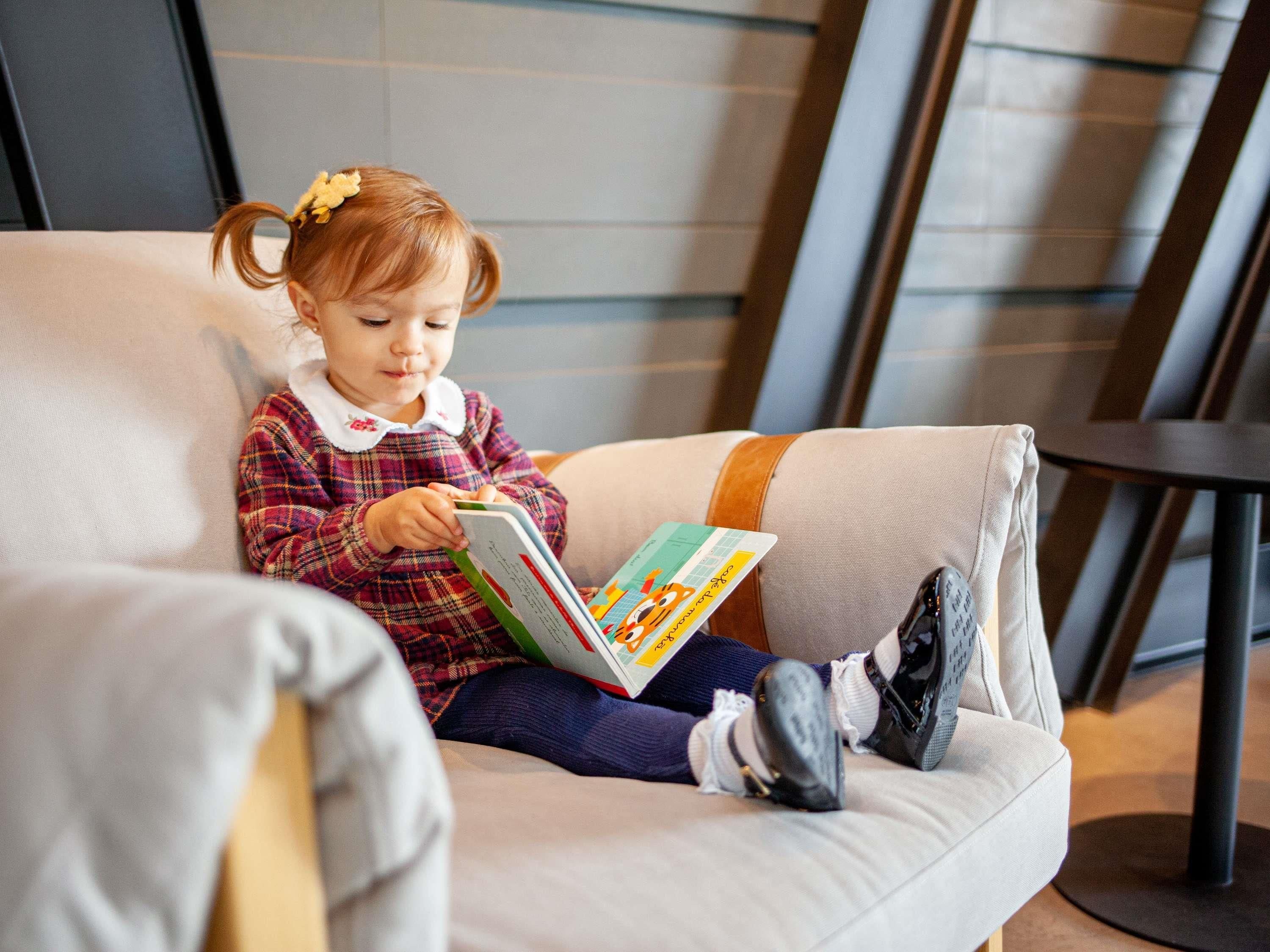 A child sitting on a cushioned chair reading a book.