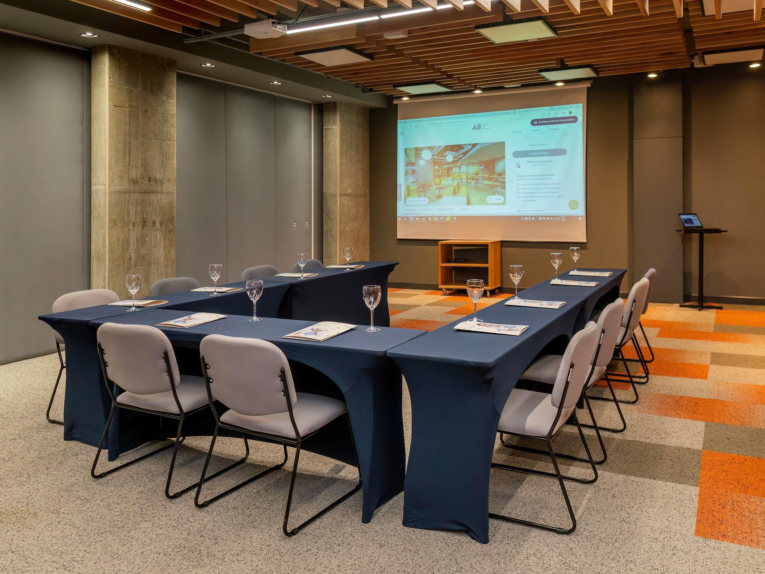 Ein Konferenzraum mit einem langen Tisch, Stühlen und einer Projektionsleinwand, die eine Präsentation zeigt.