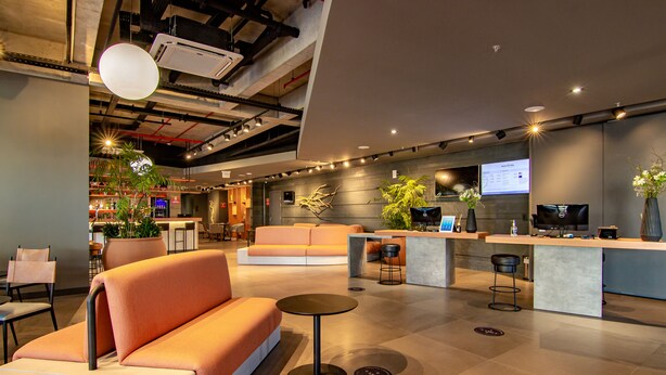 A modern lobby with a reception desk, seating area, and a large plant. - Novotel Criciuma (Criciuma)