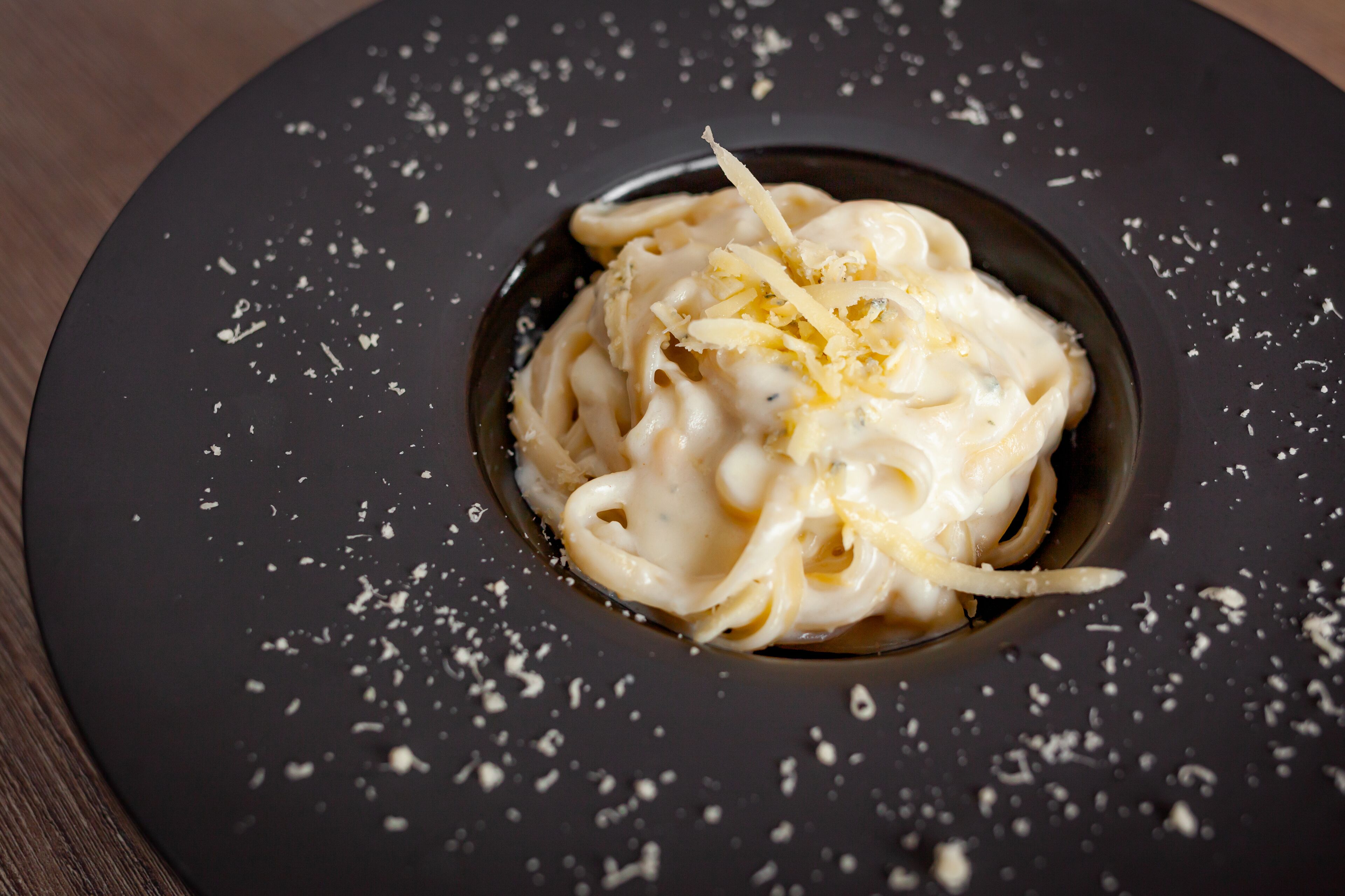 Un plato de pasta con queso rallado sobre un plato oscuro.