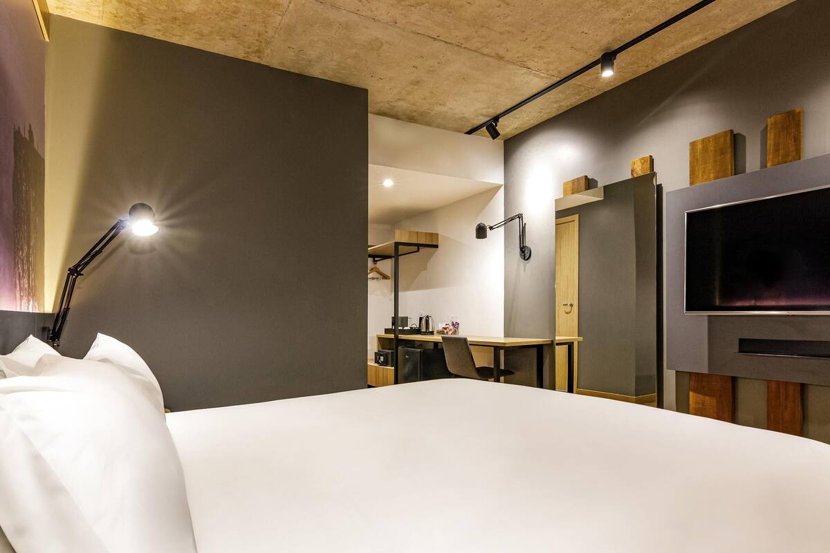 Moderni hotellihuone, jossa on suuri sänky, työpöytä, tuoli, taulutelevisio ja vaatekaappi.