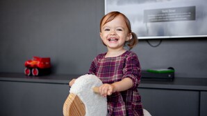 A child playing with a white toy horse in a room with a grey wall, a shelf with toys, and a framed picture. - Novotel Criciuma (Criciuma)