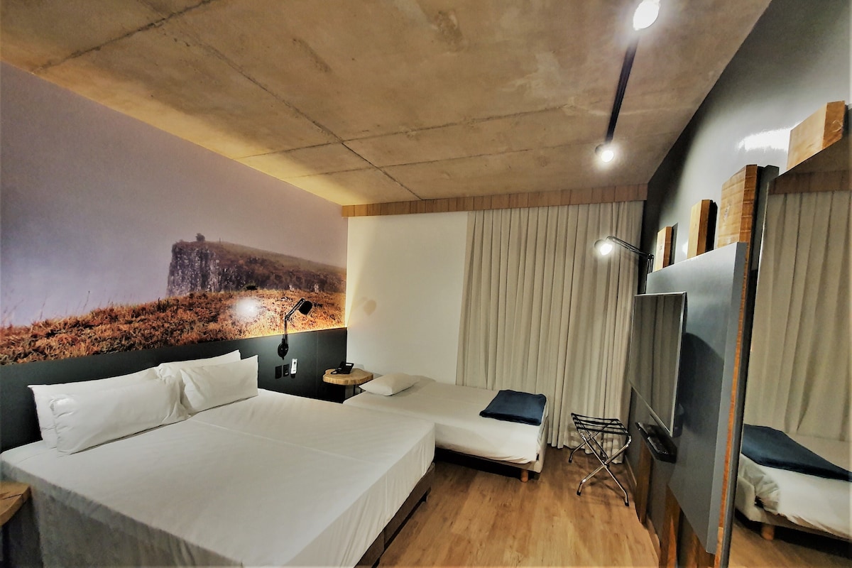 A hotel room with two beds, a large mural on the wall, a ceiling light, and a TV on the wall.
