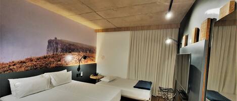 A hotel room with two beds, a large mural on the wall, a ceiling light, and a TV on the wall.