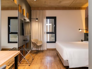 A modern hotel room with a bed, a desk, a chair, a TV, and a window with blinds. - Novotel Criciuma (Criciuma)