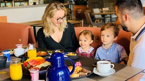 A family dining at a restaurant with a table set for breakfast, including various pastries, fruits, and beverages. - Novotel Criciuma (Criciuma)