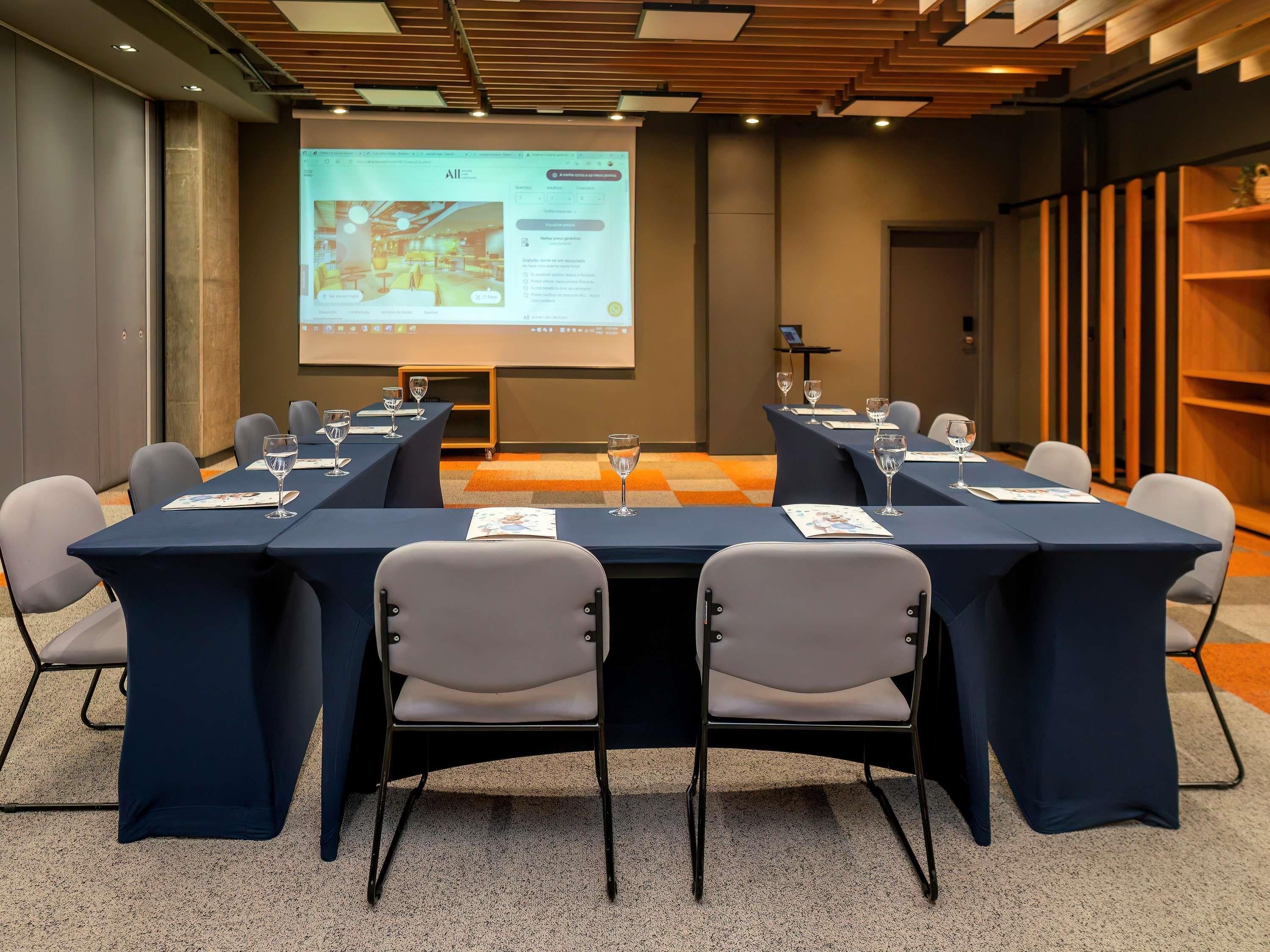 A conference room with tables, chairs, and a projection screen displaying a presentation.