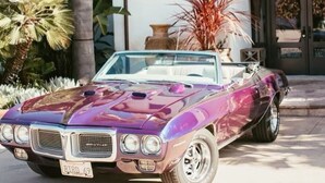 A classic purple convertible car parked in front of a building with a sign reading "Hacienda House."