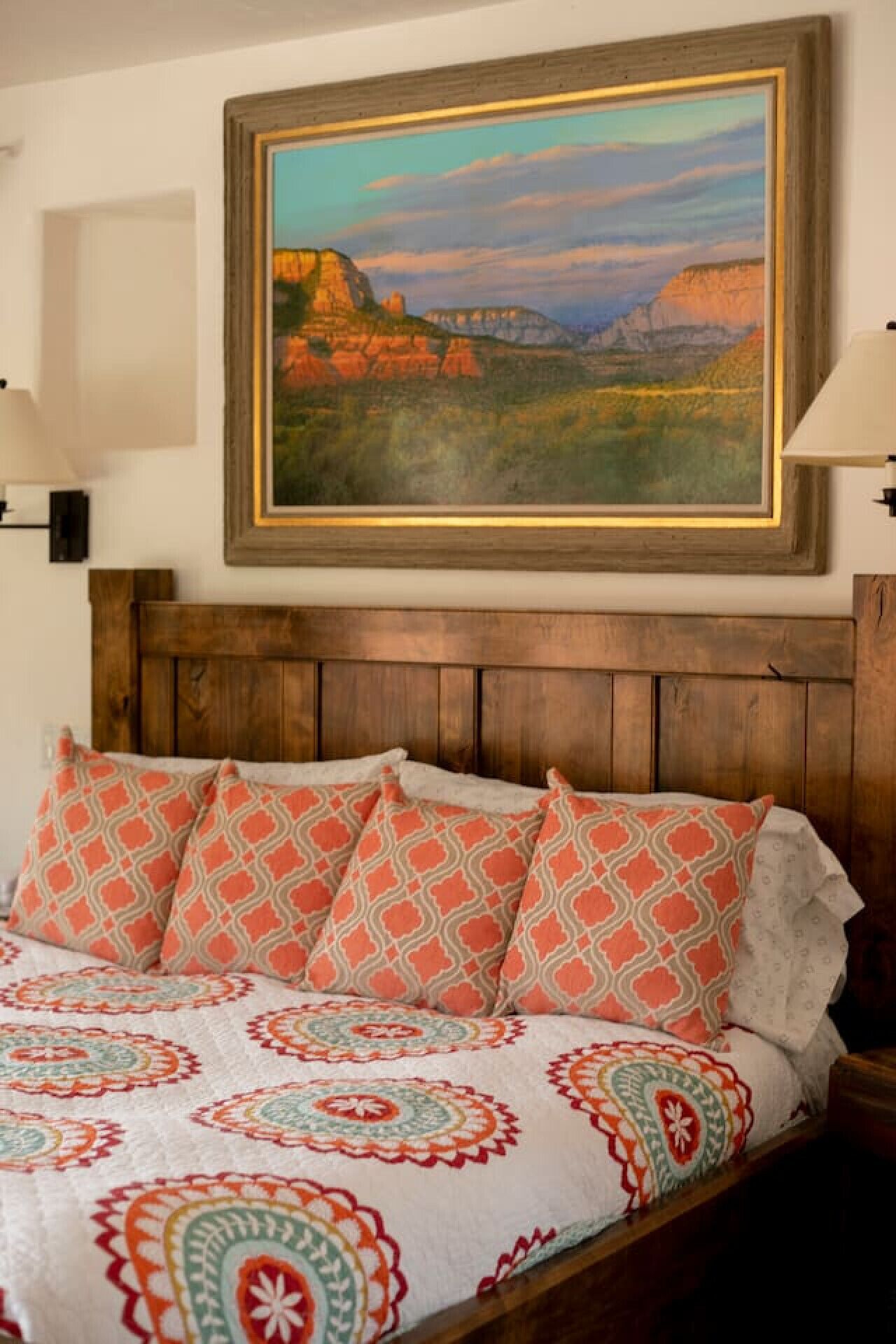 Una cama con almohadones estampados y un cuadro de un paisaje colgado encima.