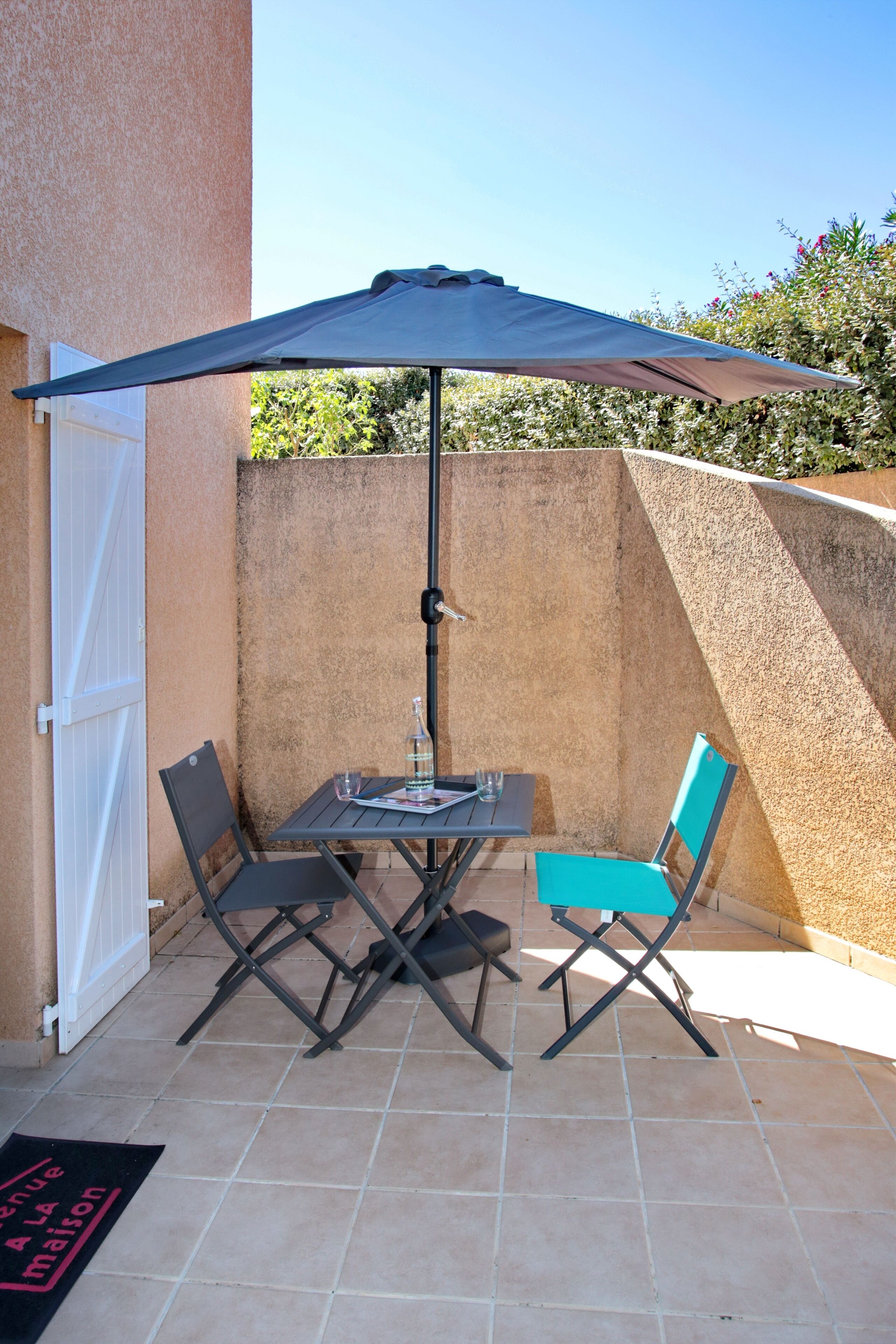 Een terras met een tafel, stoelen en een parasol, plus een deur.