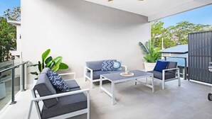 A modern outdoor patio with white furniture, a ceiling fan, and potted plants.