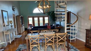 Un comedor espacioso con una mesa y sillas de madera, una lámpara de araña grande y una escalera de caracol.