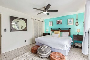 A bedroom with a bed, a ceiling fan, a mirror, a nightstand, a lamp, and a wall with framed pictures. - Sunset @ ASU | Pool, BBQ,  Game Room Near Campus (Tempe)