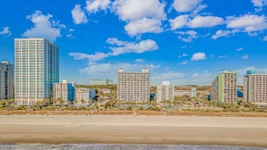 Ein Strandhotel mit mehreren Hochhäusern, einem Sandstrand und Meereswellen.