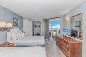 Een hotelkamer met twee bedden, een televisie, een dressoir en een balkon met uitzicht op het strand.