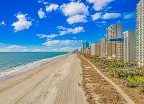 A beach with a clear sky, a sandy shore, and high-rise buildings along the coastline.