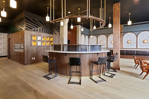 A modern bar area with wooden accents, bar stools, and pendant lighting. - Roami at The Brassline (New Orleans)