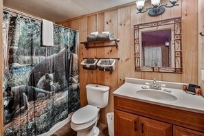 Bathroom features a large mirror, wooden vanity with sink, and shower curtain with a nature print.