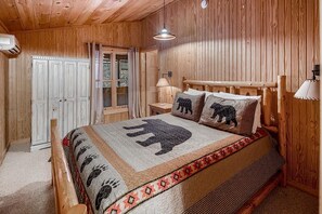 Cozy bedroom with a large bed, quilted headboard, and matching bedspread, featuring a nightstand and table with lamps.