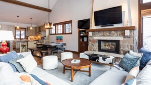 A spacious living area with a stone fireplace, a large flat-screen TV mounted above it, and a cozy seating arrangement including a sofa and ottoman. - Luxurious Ski-in Ski-out Home in Arrowhead community (Edwards)
