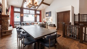 A spacious dining area with a large wooden table and multiple chairs, a stone fireplace, and a view of the outdoors through large windows. - Luxurious Ski-in Ski-out Home in Arrowhead community (Edwards)