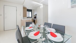 Un espace repas moderne avec une table en verre dressée pour six personnes, des assiettes blanches et des serviettes rouges.