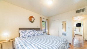 Une chambre à coucher avec un grand lit, une table de chevet, une horloge murale et une porte donnant sur une autre pièce.