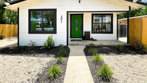 A single-story house with a white exterior and black trim, featuring a green door and two windows on the front. - *Just off River Trail, Bikes, Fire Pit, Hot Tub* (Kerrville)