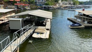 A dock with a covered boat ramp, a small boat, and a row of houses along the water. - Waterfront Cottage & Dock w/ Beautiful View - 5MM (Rocky Mount)