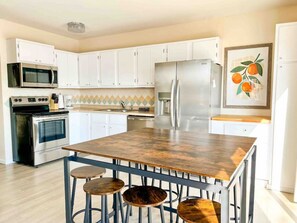 A modern kitchen with white cabinets, a stainless steel refrigerator, a microwave, an oven, and a wooden island with stools. - Waterfront Cottage & Dock w/ Beautiful View - 5MM (Rocky Mount)