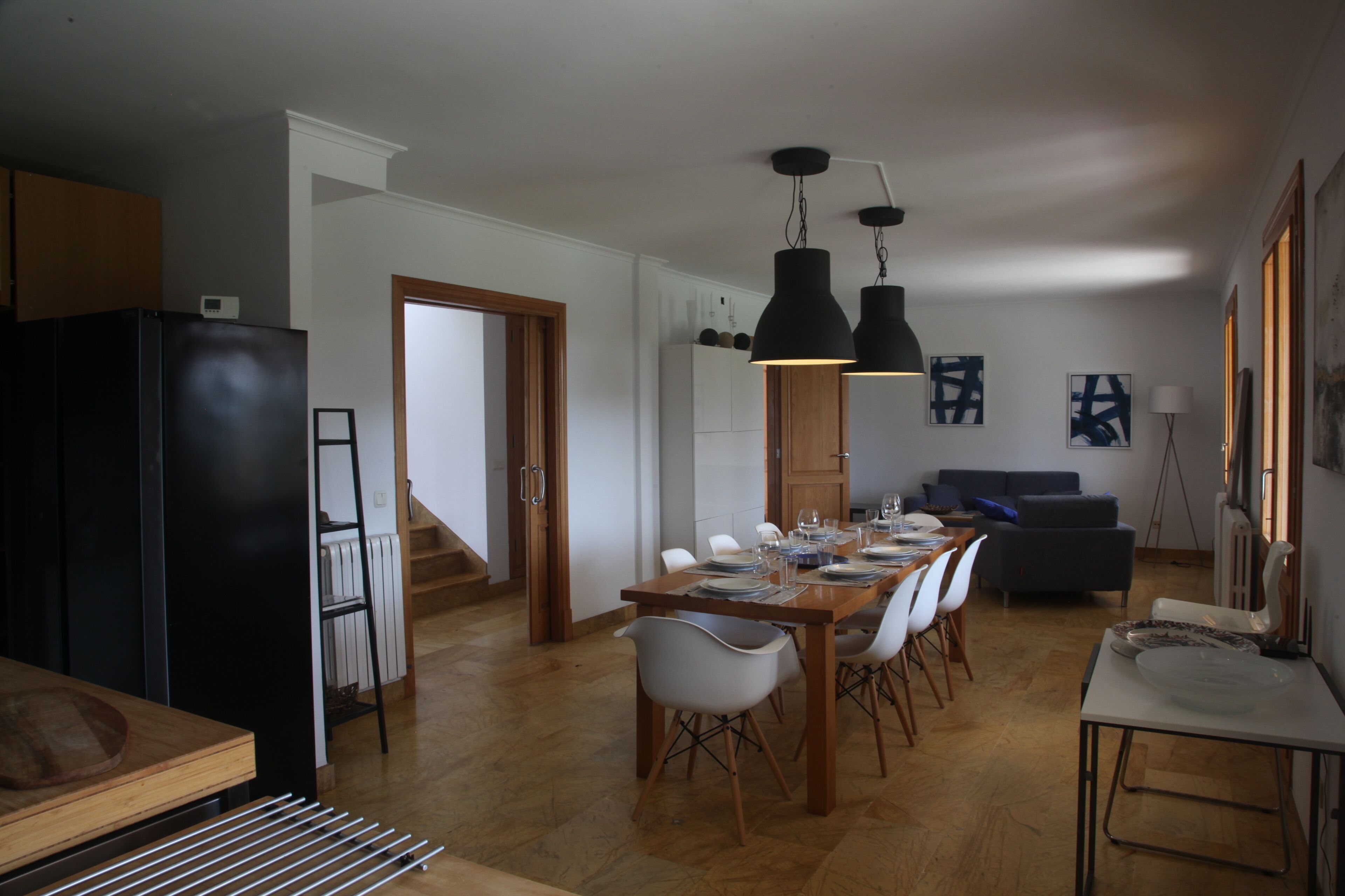 A modern kitchen with a black refrigerator, wooden cabinets, and a dining area with a long table and chairs.