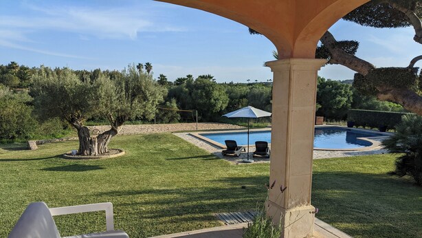 Eine Terrasse mit weißem Tisch und zwei Stühlen, ein Schwimmbad und ein überdachter Bereich mit einer Pergola.