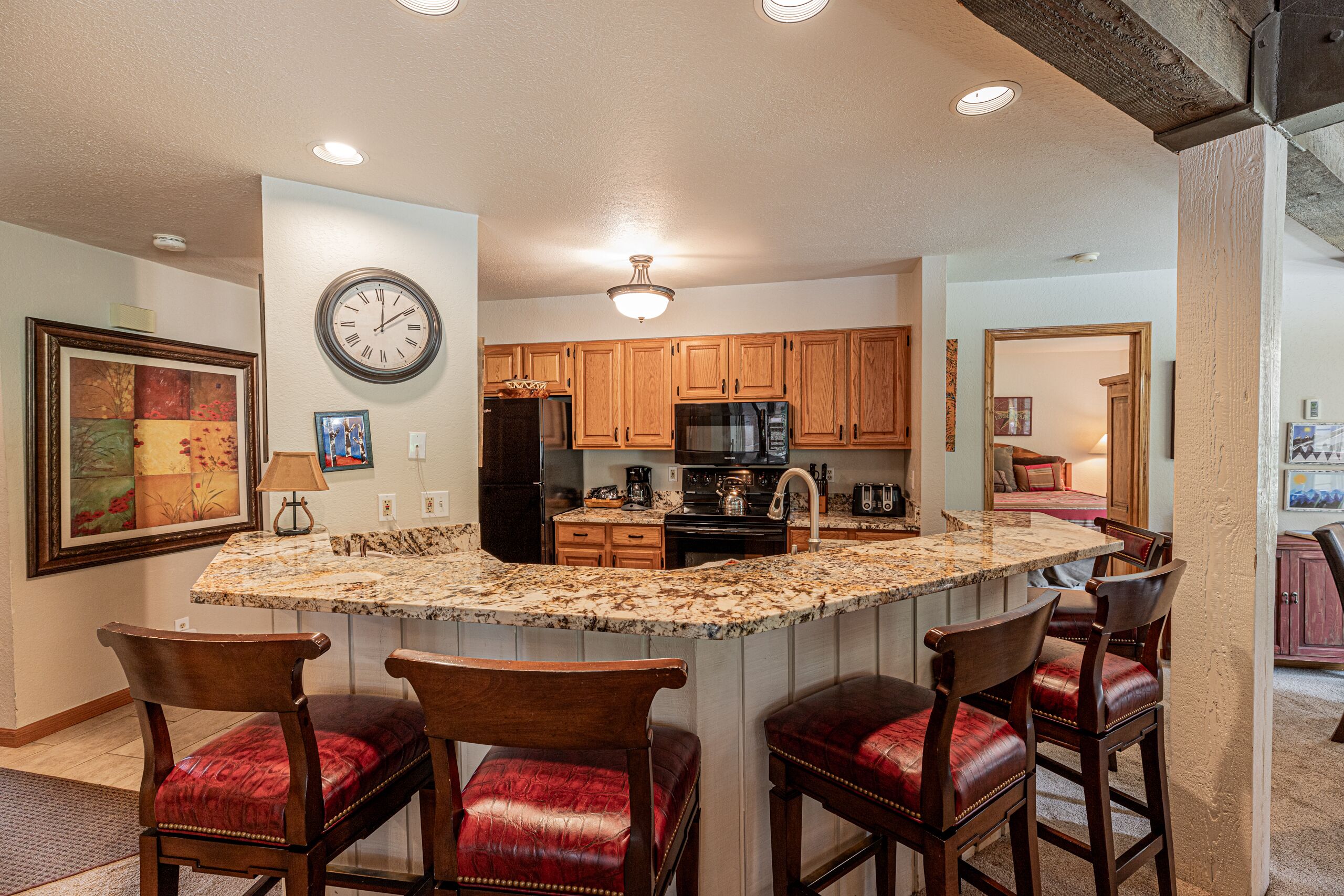 A kitchen with wooden cabinets, a granite countertop, and a clock on the wall.