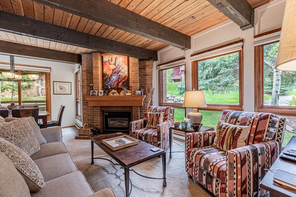 A cozy living room with a fireplace, comfortable seating, and large windows offering a view of the outdoors. - Stylish 3BR | Walk to the Slopes | Pool, Hot Tubs, and More! (Steamboat Springs)