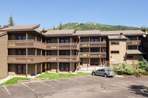 A multi-story hotel with balconies, a parking lot, and a mountainous backdrop. - Stylish 3BR | Walk to the Slopes | Pool, Hot Tubs, and More! (Steamboat Springs)