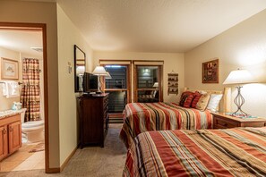 A bedroom with two beds, a dresser, a mirror, and a bathroom visible through an open door. - Stylish 3BR | Walk to the Slopes | Pool, Hot Tubs, and More! (Steamboat Springs)