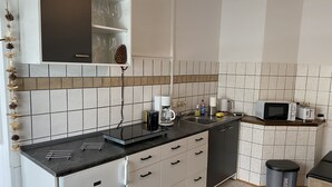 A compact kitchen with white cabinets, a black countertop, and a microwave. - Apartment "Squirrel" in the middle of the Thuringian Forest (Suhl)