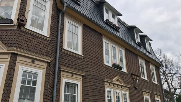 A multi-story building with a brown tiled exterior, white window frames, and a visible chimney. - Apartment "Squirrel" in the middle of the Thuringian Forest (Suhl)