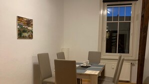 A dining area with a table and four chairs, a window with a view of the sky, and a painting on the wall. - Apartment "Squirrel" in the middle of the Thuringian Forest (Suhl)