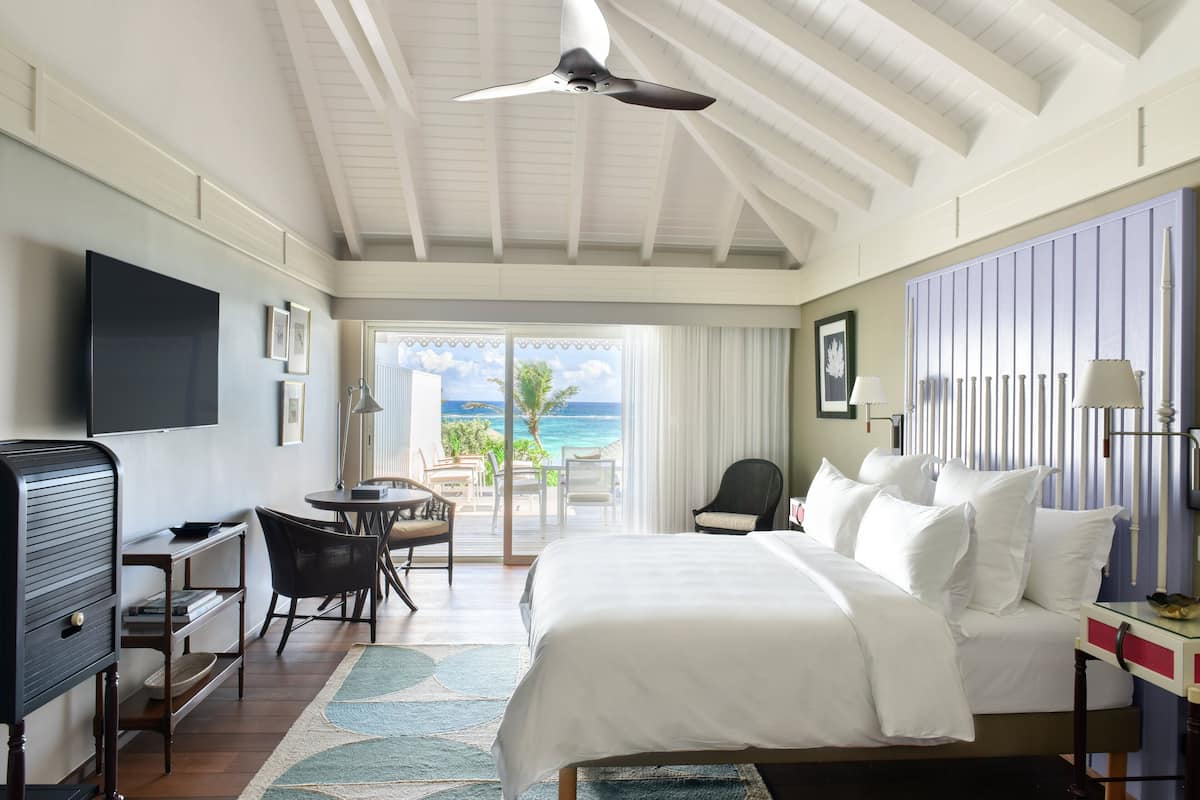 A hotel room with a bed, a desk, a chair, a television, and a view of the ocean.