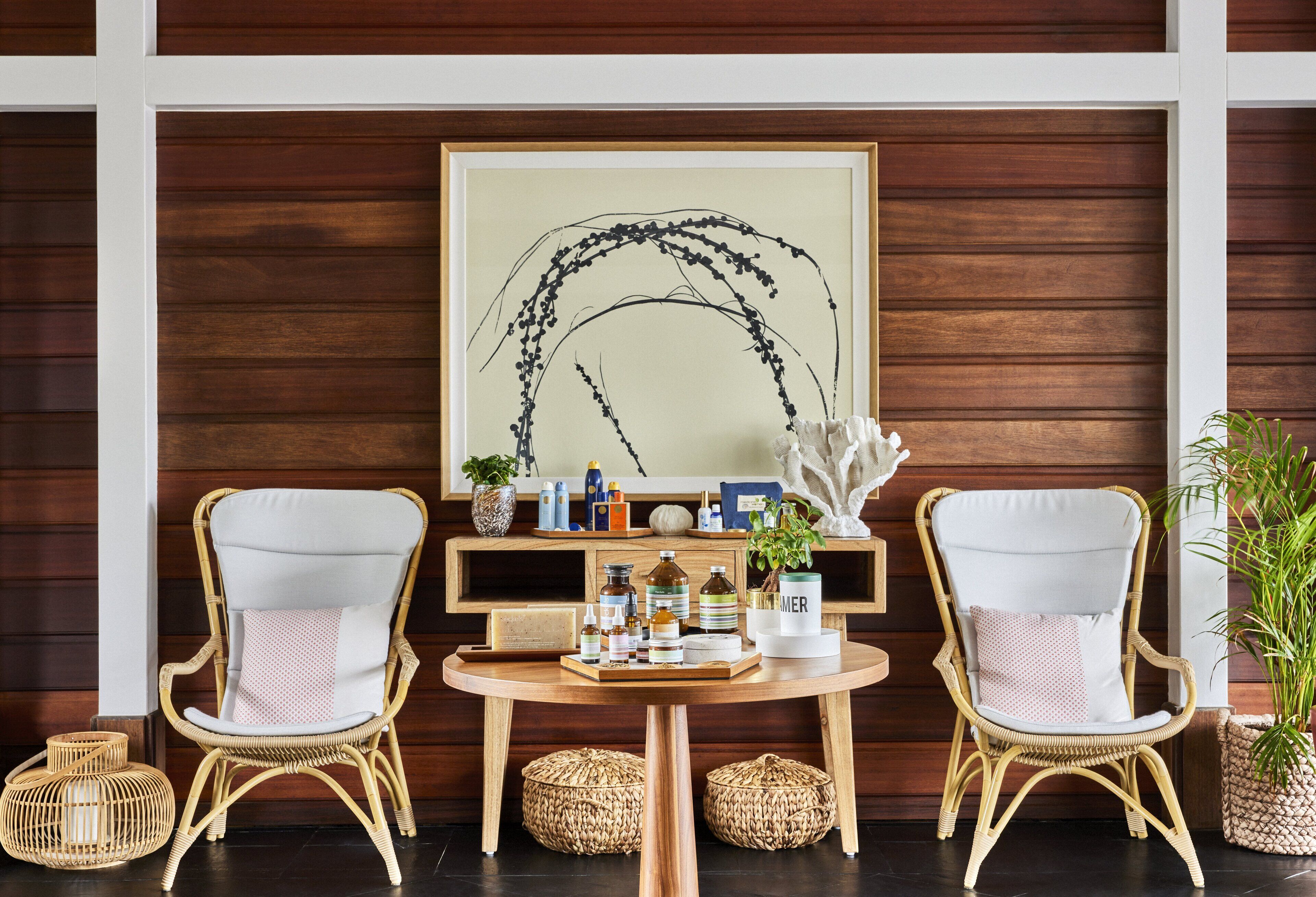 A room with two wicker chairs, a small round table, and a wooden wall with a framed artwork.