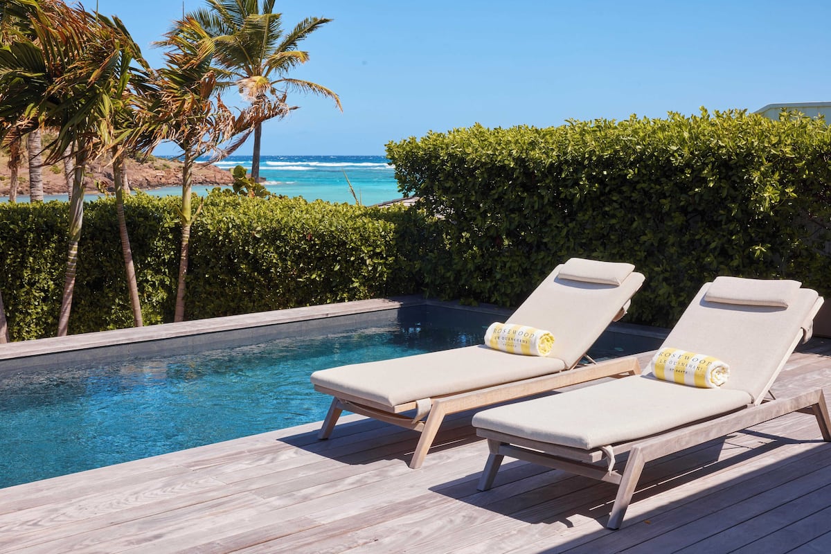 A poolside area with two lounge chairs, a wooden deck, and a view of the ocean.