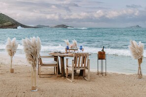 A beachside table set with chairs, pampas grass, and a bottle of wine, overlooking the ocean. - Rosewood Le Guanahani St Barth (St. Barthelemy)