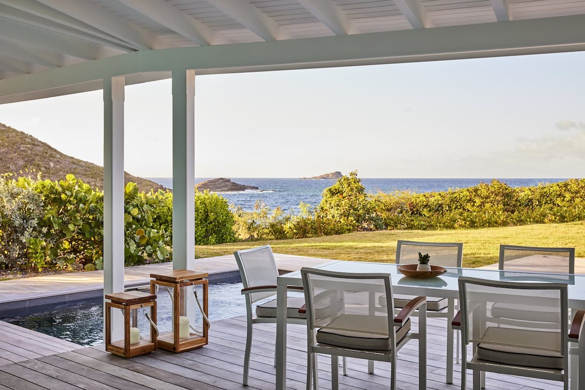 A covered outdoor seating area with a pool, overlooking a coastal landscape.