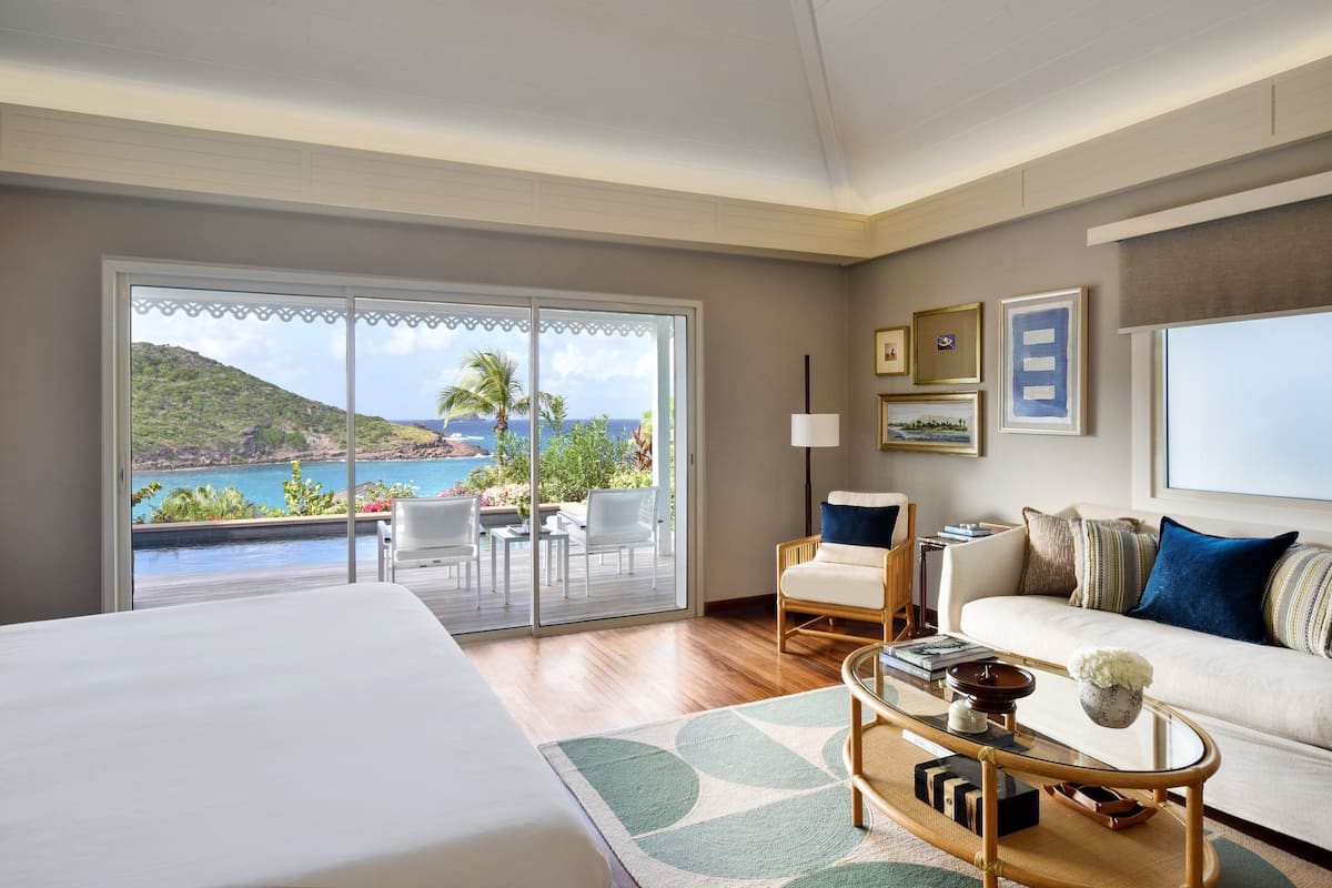 A hotel room with a large bed, a sofa, a coffee table, and a view of a pool and mountains.