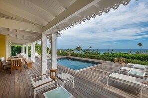 A wooden deck with a pool, lounge chairs, and tables overlooking a beach. - Rosewood Le Guanahani St Barth (St. Barthelemy)