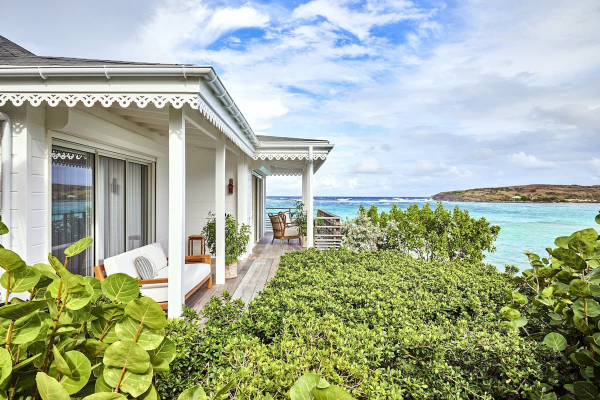 A white building with a covered porch overlooking a beach.