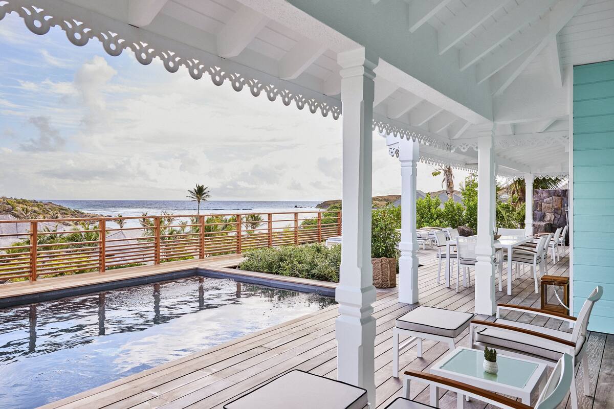 A covered outdoor area with a pool, seating, and a view of the ocean.
