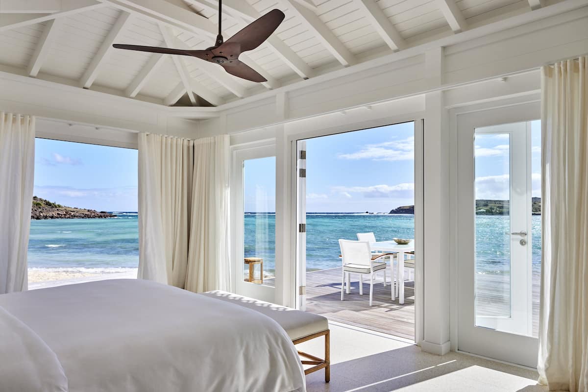 A bedroom with a large bed, a ceiling fan, and a view of the ocean through large windows.